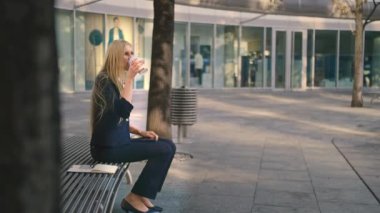 Kahve ve tablet bankta kadınla. Tablet bankta oturuyor ve içme kahve ikindilerde uzakta içinde eğlence arıyor resmi kadın yan görünüm.