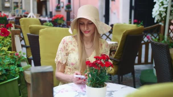 Frau surft Smartphone in außerhalb Café. Fröhliche Frau sitzt am Tisch im Restaurant und surft im Smartphone. — Stockvideo