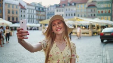 Kadın kareye selfie çekiyor. Çekici kadın selfie için poz veriyor ve şehir meydanında duruyor..