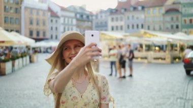 Kadın kareye selfie çekiyor. Çekici kadın selfie için poz veriyor ve şehir meydanında duruyor..