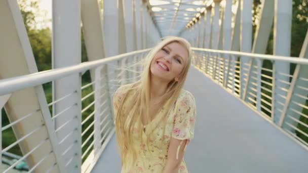 Een vrouw kijkt terug op de brug. Mooie blonde vrouw kijkt terug op de camera tijdens het lopen op de brug met golvend haar. — Stockvideo