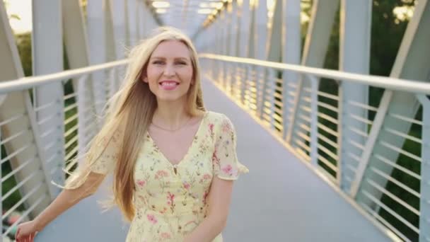 Mujer mirando hacia atrás en el puente. Mujer rubia bonita mirando hacia atrás a la cámara mientras se ejecuta en el puente con el pelo ondulado. — Vídeos de Stock