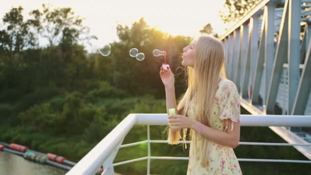 Woman blowing soap bubbles. Side view of pretty woman blowing soap bubbles while standing on pedestrian bridge. — Stock Video