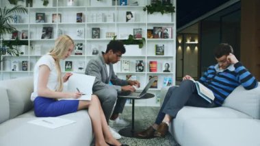 Siyahi adam iş arkadaşlarıyla iyi haberleri paylaşıyor. Afro-Amerikalı adam dizüstü bilgisayarda sörf yapıyor ve harika haberleri iş arkadaşlarıyla paylaşıyor. Masanın etrafında birlikte oturuyorlar..