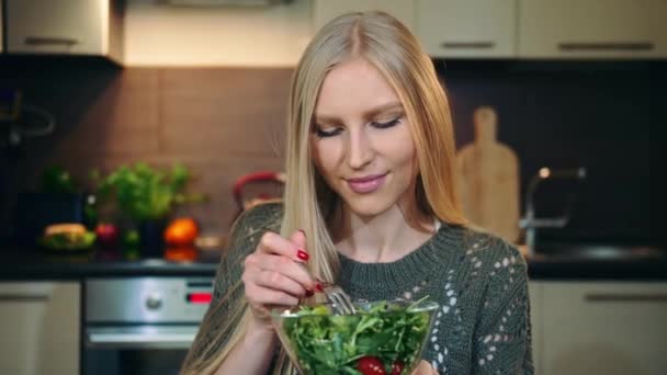 Frohe Frau, die gesunden Salat isst. Schöne junge Frau genießt gesunden Gemüsesalat und blickt in die Kamera, während sie in der stilvollen Küche sitzt. — Stockvideo