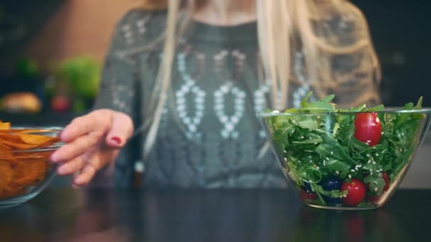 Jeune femme préférant la salade à croustillante. Belle jeune femme choisissant de manger croustillant sain pour le souper tout en étant assis à la table dans une cuisine élégante et elle mange ces salades . — Video