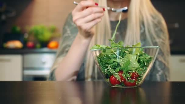 İyi ki kadın sağlıklı salata yiyor. Güzel genç bayan sağlıklı sebze salatasının tadını çıkarıyor ve şık bir mutfakta oturmuş kameraya bakıyor.. — Stok video