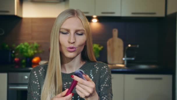 De jonge vlogger heeft het over make-up borstel. Aantrekkelijke jonge vrouw praten over zachte cosmetische borstel tijdens het schieten video voor schoonheid vlog in de keuken. — Stockvideo