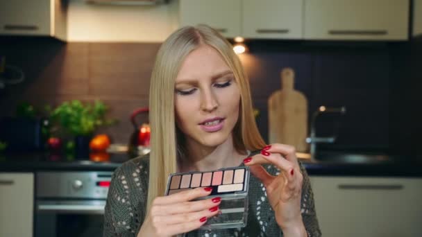 Ung vlogger pratar om makeup ögonskugga. Attraktiv ung kvinna talar om kosmetisk ögonskugga medan du spelar in video för skönhet vlog i köket. — Stockvideo