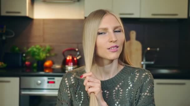 Ung vlogger kammar hår för kamera. Söt ung kvinna borsta blont hår med kam medan du filmar video för skönhet vlog i mysigt kök. — Stockvideo