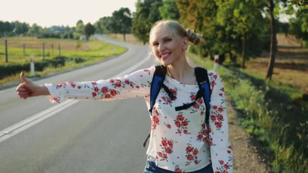 Mujer viajera haciendo autostop en un camino soleado y caminando . — Vídeos de Stock