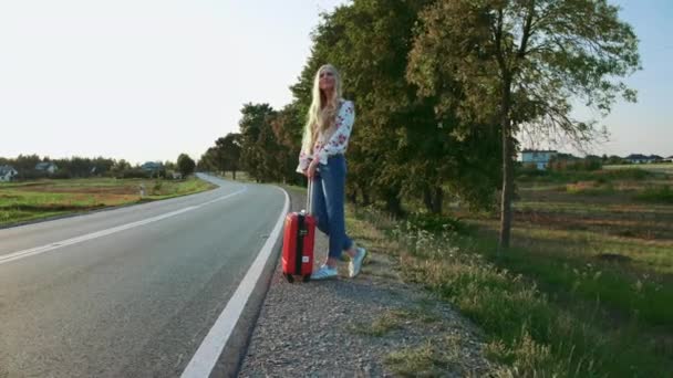 Reiziger vrouw liften op een zonnige weg en wandelen. — Stockvideo