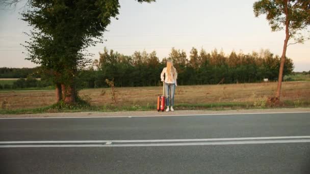 Ung kvinna liftar på landsbygden väg. — Stockvideo