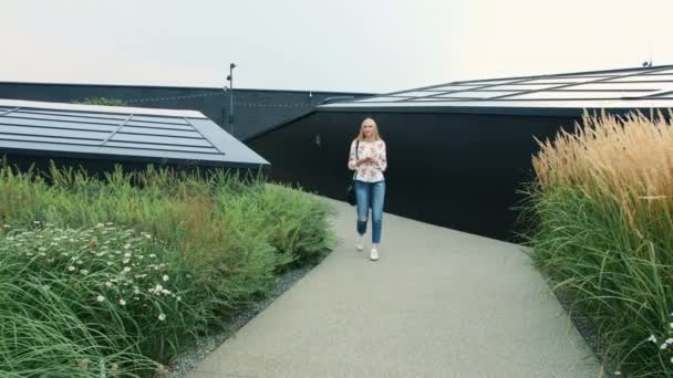 Woman with smartphone walking on green roof of mall. — Stock Video