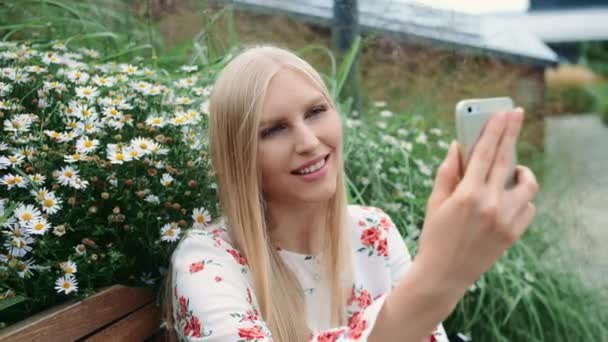 アメリカの巨大なモールの生活屋根の上にベンチに座っている間にビデオ通話を行うためにスマートフォンを使用して素敵な若い女性. — ストック動画