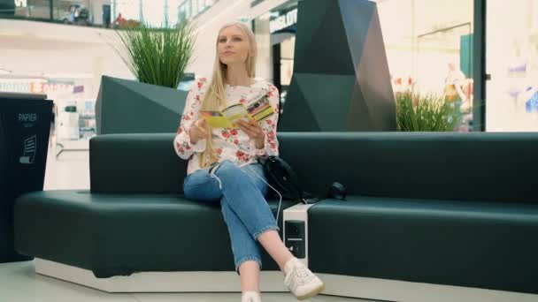Woman recharging smartphone and reading flyer in mall. — Stock Video
