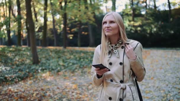 Młoda dziewczyna, chodzenie w jesienny Park i SMS-y wiadomość na telefon komórkowy — Wideo stockowe