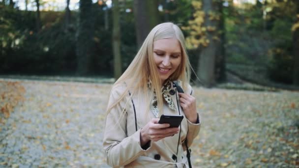 Chica rubia joven caminando en el parque de otoño y lanzando hojas doradas en el aire, cámara lenta — Vídeo de stock