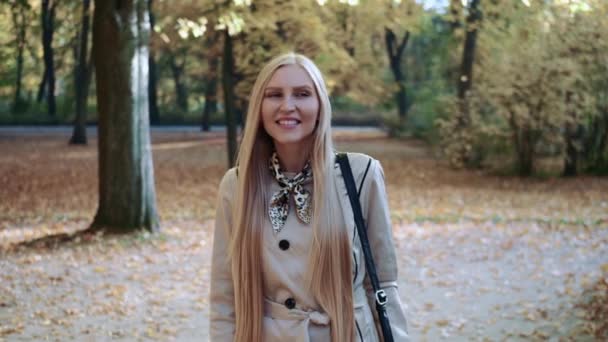 Mooi jong blond meisje wandelen in het park in de herfst en glimlachen — Stockvideo