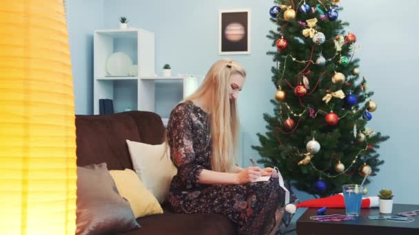 Mulher bonita escrevendo um postcad perto da árvore de Natal — Vídeo de Stock