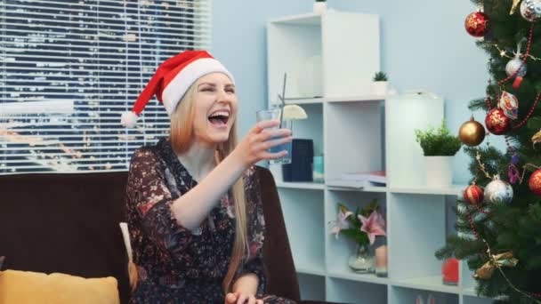 Nahaufnahme einer lächelnden Frau mit Weihnachtsmannhut, die Toast anstößt und Cocktail trinkt — Stockvideo
