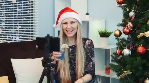 Primer plano de la hermosa joven en Santa sombrero de rodaje de un video blog por teléfono inteligente en casa — Vídeo de stock