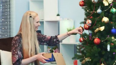 Neşeli bir kadın Noel ağacına oyuncak asar ve onları kutusundan çıkarır.