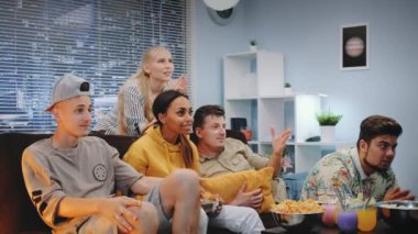 Mutlu izleyiciler televizyonda maç seyrediyor ve takım sayı yaptığında patlamış mısır döküyorlar.