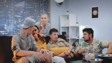Yakışıklı erkekler ve kadınlar evde sohbet ediyor ve TV 'de eylem tartışıyorlar.
