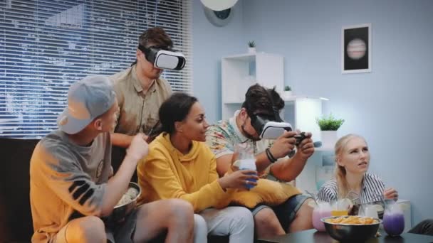 Zwei gutaussehende Jungen spielen Konsolenspiel in Virtual-Reality-Brille in fröhlicher Gesellschaft — Stockvideo