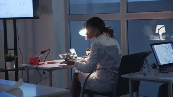 Задний вид женской электроники, проверяющей материнскую плату с помощью тестера мультиметра — стоковое видео