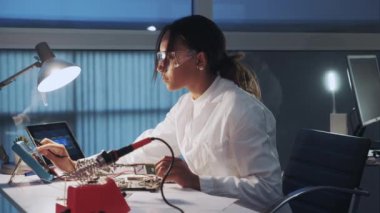 Laboratuvarda çoklu ölçüm cihazı ve diğer elektronik cihazlarla çalışan Afrikalı Amerikan elektronik uzmanının yan görüntüsü