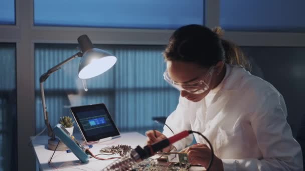 Mellan närbild av kvinnlig ingenjör av elektronik i vit rock och skyddsglasögon kontroll moderkort med multimeter testare — Stockvideo