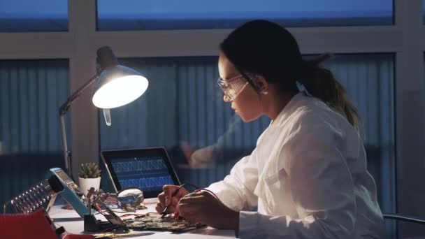 Ingeniera de electrónica femenina que trabaja con probador de multímetros y otros dispositivos electrónicos en laboratorio — Vídeos de Stock