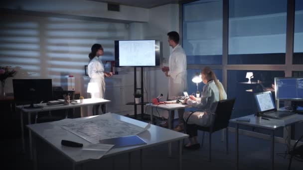 Équipe d'ingénieurs informatiques discutant de quelque chose sur un grand écran de télévision dans le laboratoire 
