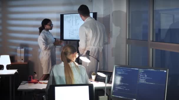 Spécialistes multiraciaux en électronique parler quelque chose et montrer sur un grand écran de télévision dans le laboratoire 