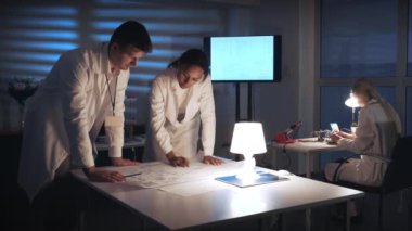 Beyaz önlüklü melez mühendisler laboratuvarda elektronik kontrol şemasını tartışıyorlar.