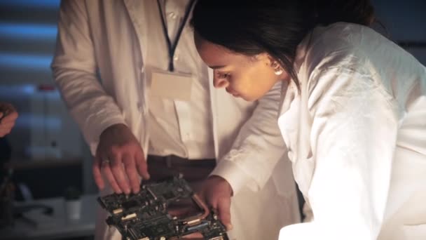 Primo piano della donna afro-americana in camice da laboratorio che discute della costruzione della scheda madre con altri ingegneri — Video Stock