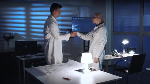 Два инженера-электроника в белых халатах, протягивающие руку приветствия встречаются, чтобы рассказать о своей работе. — стоковое видео