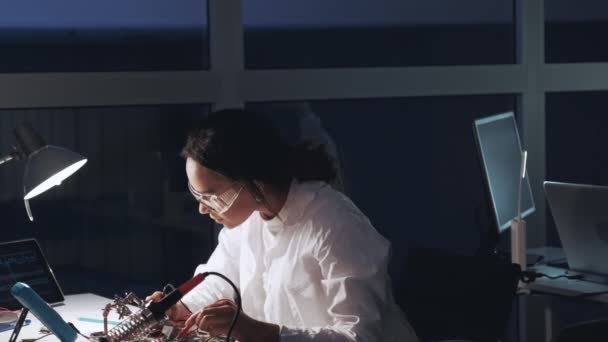 African American Electronics specialist in protective glasses and white coat work with multimeter tester and motherboard in lab — Αρχείο Βίντεο