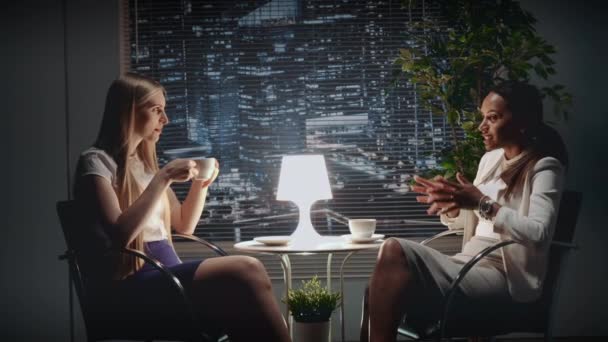 Deux jeunes femmes d'affaires parlent de quelque chose à table avec une tasse de boisson — Video