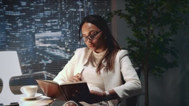Mixed race Business meisje maken van notities in haar laptop op kantoor — Stockvideo