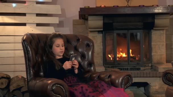 Маленька дівчинка в гарній сукні спілкується з друзями за допомогою смартфона ввечері вдома — стокове відео