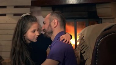 Mutlu baba ve küçük kız şöminenin yanındaki koltukta kucaklaşıyorlar.