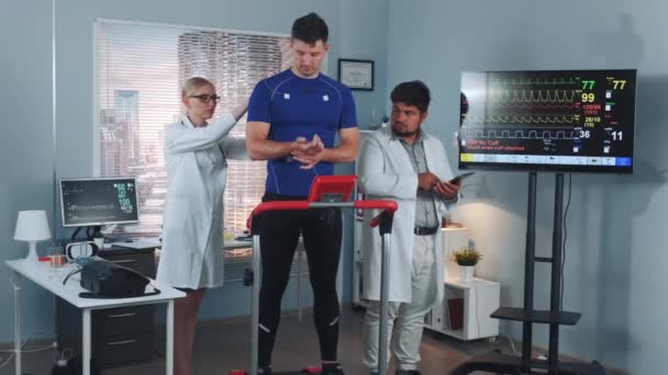 Medicina deportiva: mujer y hombre haciendo medidas en deportista fuerte en laboratorio moderno — Vídeos de Stock