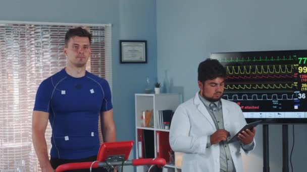 Mixed race doctor performing stress test while the athlete walking on treadmill — Stock Video
