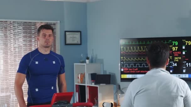 Etlete guapo que está siendo probado y monitoreado por el médico multirracial durante la prueba de cinta de correr en el laboratorio — Vídeos de Stock