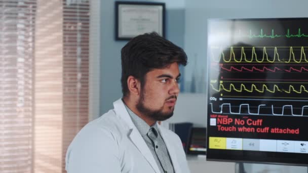 Close-up van mixed race Doctor Learning ekg-gegevens toonden op grote display — Stockvideo