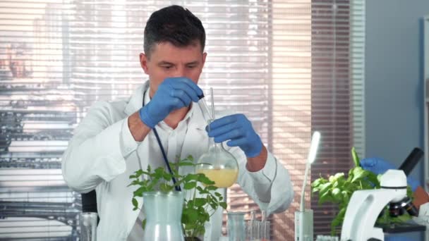 In een laboratorium voor chemisch onderzoek mengt een wetenschapper twee verbindingen in een kolf met behulp van pipet — Stockvideo