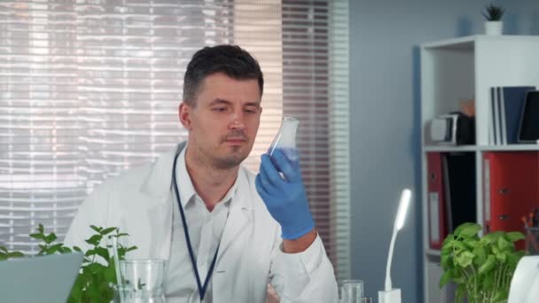 Científico investigador guapo observando la reacción líquida en frasco cónico durante el experimento — Vídeo de stock